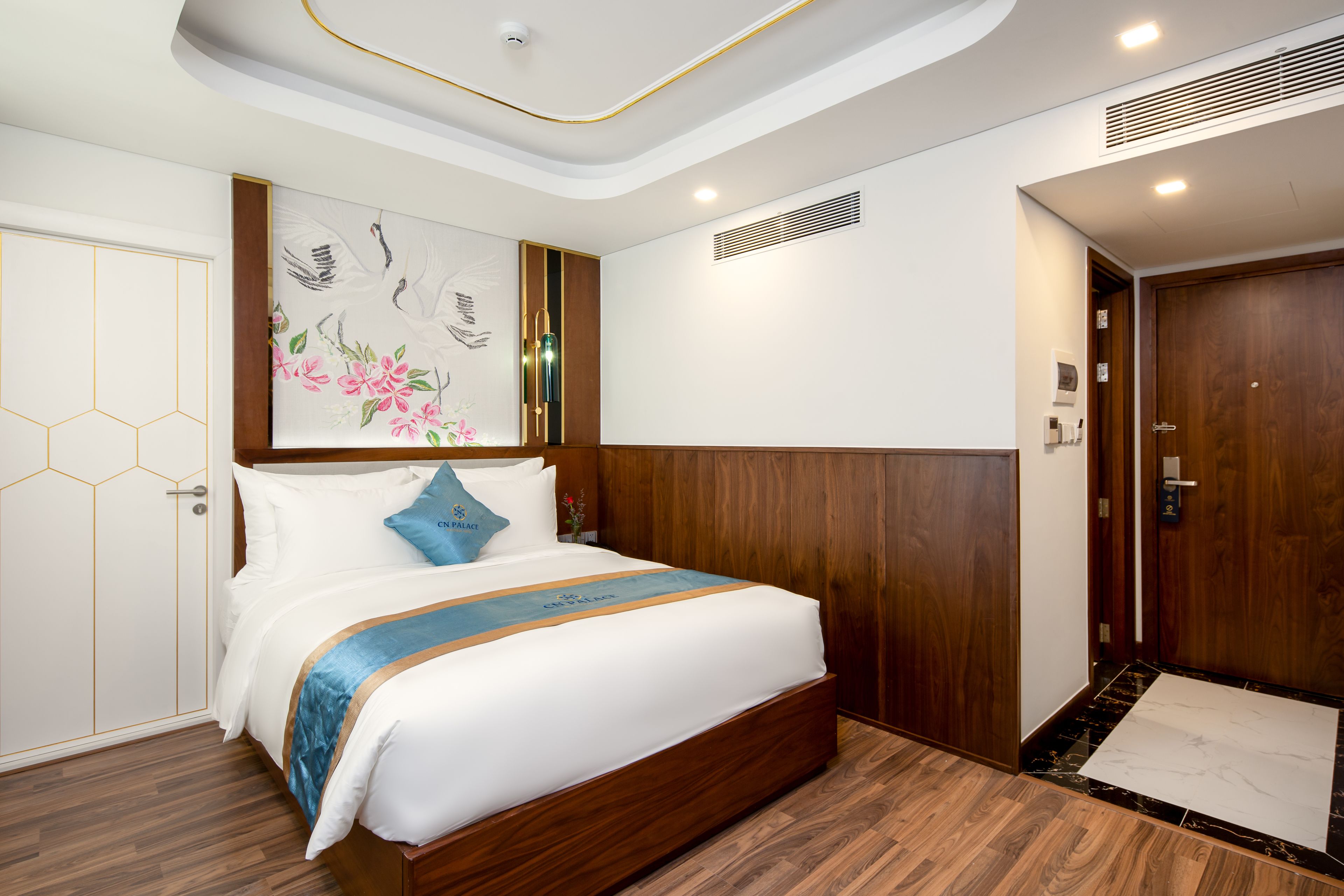 A hotel room with a wooden bed, a large painting on the wall, and a wooden door.