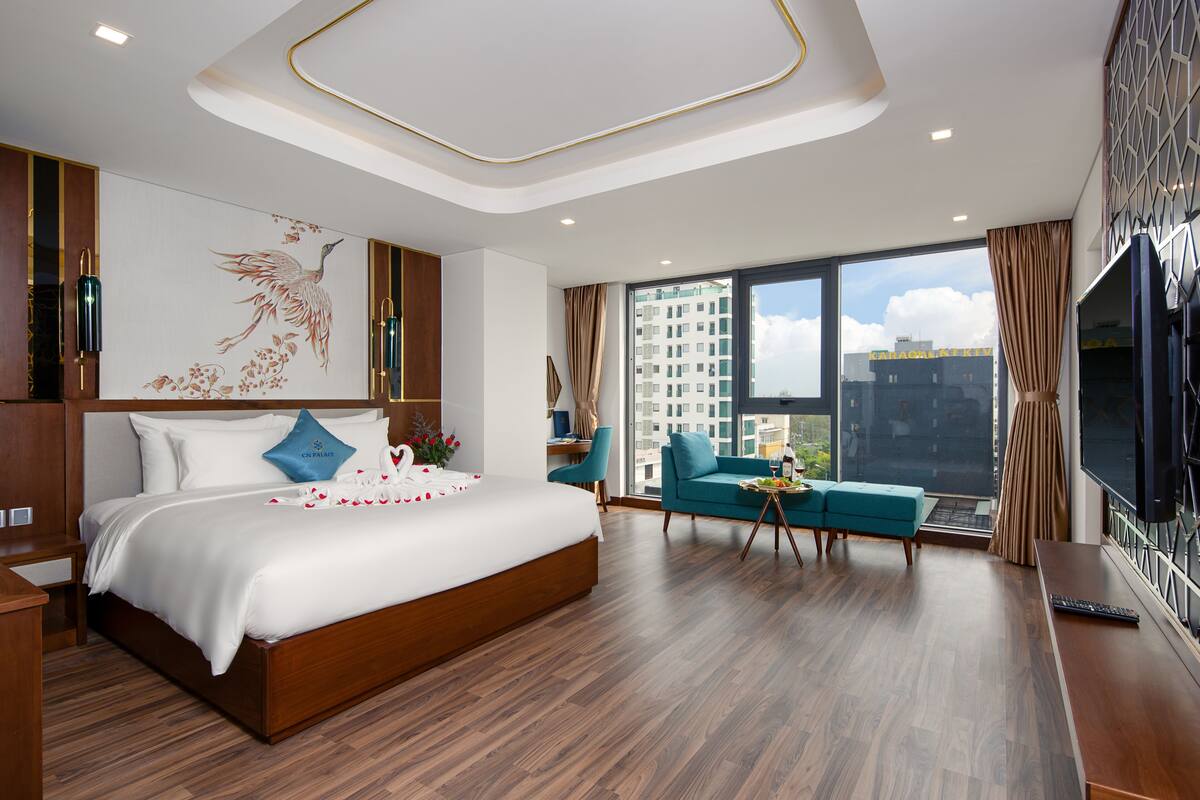 A modern hotel room with a large bed, a sofa, a TV, and a city view.
