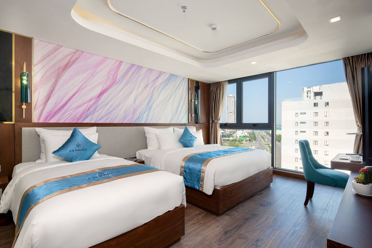 A hotel room with two beds, a large window with a view of buildings, and a modern ceiling design.