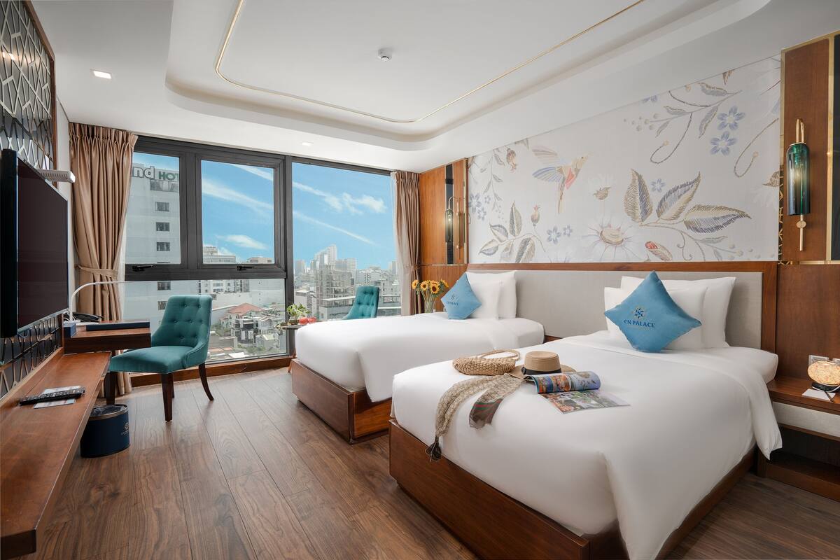 A hotel room with two beds, a desk, a chair, a TV, and a city view.