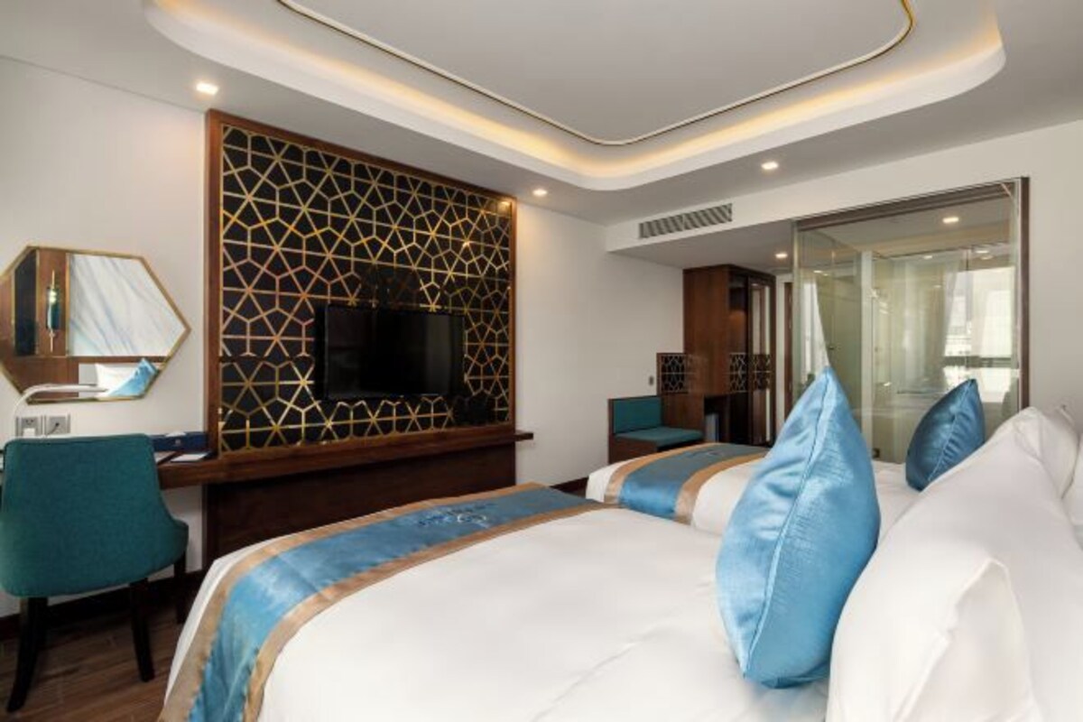 A hotel room with a large bed, a desk with a chair, a TV, and a decorative wall panel.