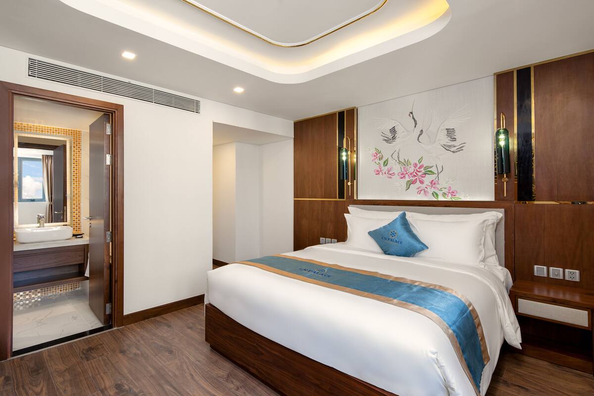 A modern hotel room with a large bed, wooden headboard, and a wall-mounted artwork.