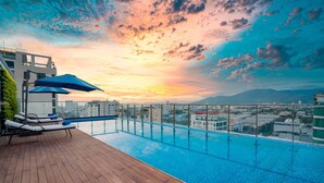 A rooftop infinity pool with lounge chairs and umbrellas, overlooking a cityscape at sunset. - CN Palace Boutique Hotel & Spa (Da Nang)