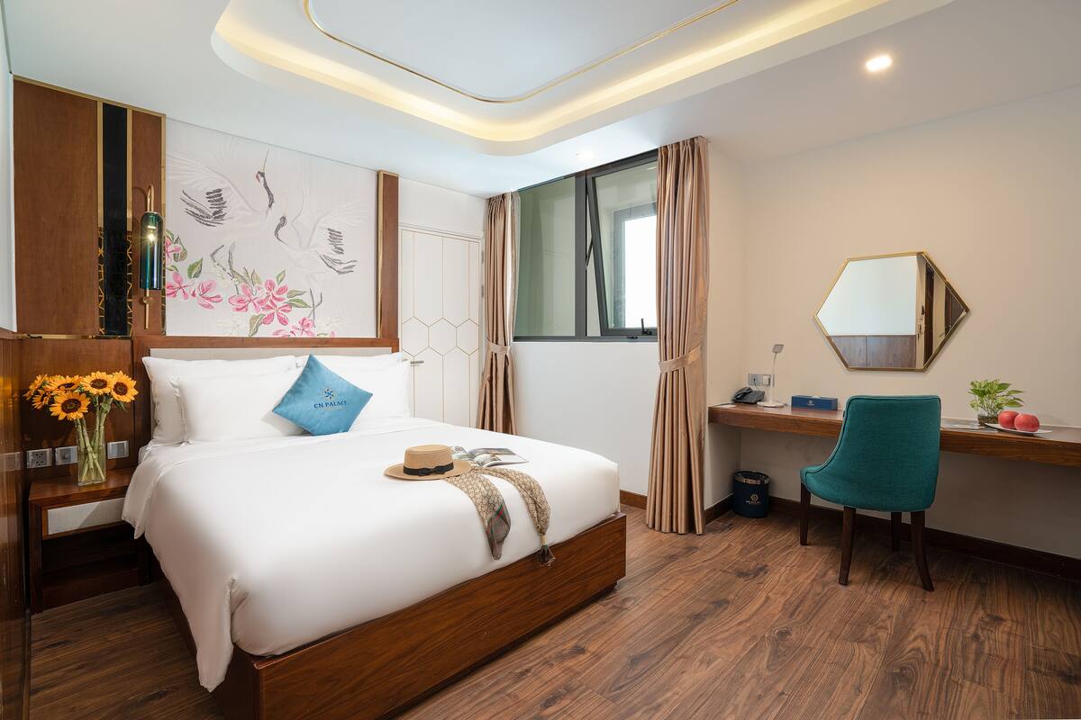 A modern hotel room with a large bed, a desk, a chair, and a large window.