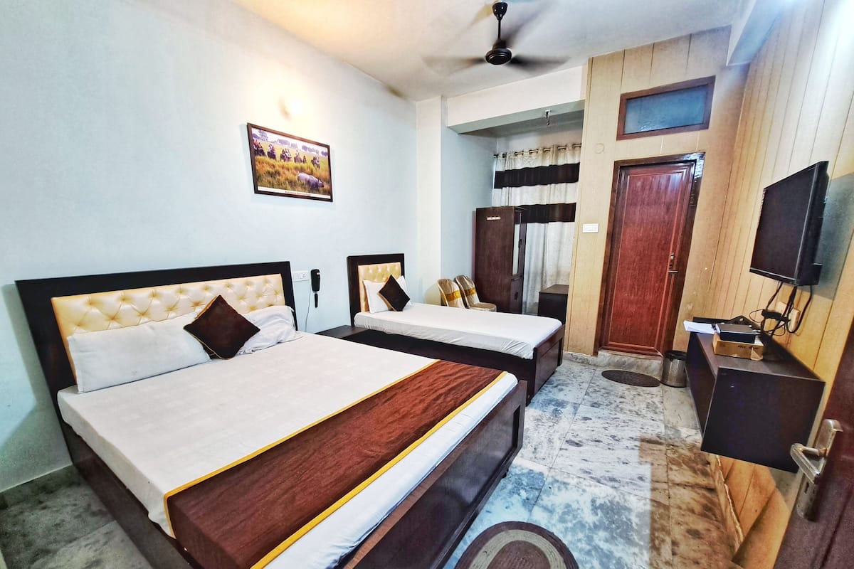 A hotel room with two beds, a TV, a ceiling fan, and a wooden wardrobe.