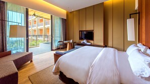 Habitación de hotel moderna con una cama grande, zona de estar, televisor y balcón con vistas al edificio.