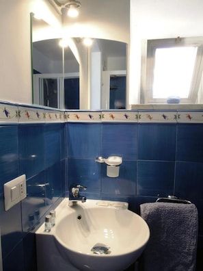 Un baño con lavamanos blanco, azulejos azules, un espejo y una ventana.