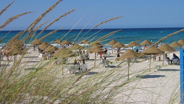 A beach with thatched umbrellas and sun loungers, a clear blue sky, and the ocean in the background. - Residence Stern (Hammam Al Agzaz)