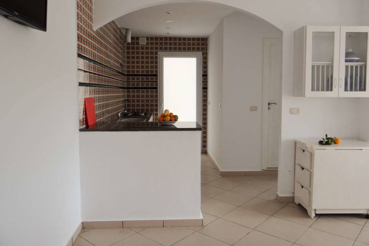 A modern kitchen with a tiled backsplash, a white countertop, and a small fruit bowl. There is a white cabinet with a glass door and a white sink.