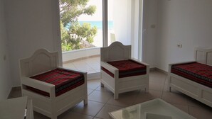 A room with three white beds with red patterned bedding, a glass table, and a view of the sea through a large window. - Residence Stern (Hammam Al Agzaz)