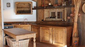 A rustic kitchen with wooden cabinets, a wooden table, and a hanging pot rack. - Chalet Fiore (Val di Zoldo)