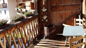 A wooden balcony with a table and chairs, potted plants, and a wicker basket. - Chalet Fiore (Val di Zoldo)