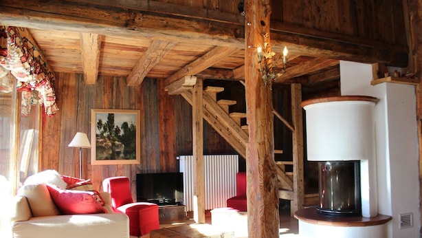 A rustic wooden interior with a sofa, red chairs, a fireplace, and a television. - Chalet Fiore (Val di Zoldo)