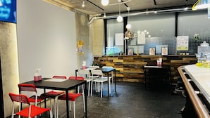 A modern cafe with wooden accents, a counter with artwork, and a seating area with tables and chairs. - Hotel Adonis - Hostel (Tokyo)
