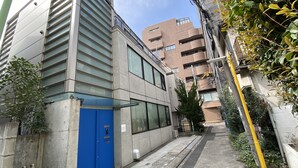 A modern building with large windows and a blue door, surrounded by greenery and other buildings. - Hotel Adonis - Hostel (Tokyo)