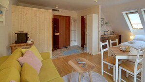 A compact, well-lit room with a bed, a small table, and a sofa. There are two windows providing natural light, and a kitchenette area is visible. - Apartament z Sauną pod Świerkami - Apartamenty 5d (Karpacz)