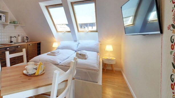 A compact room with a kitchenette, a bed with two pillows, a bedside table with a lamp, and a TV mounted on the wall. - Apartament z Sauną pod Świerkami - Apartamenty 5d (Karpacz)