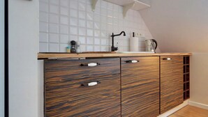 A kitchen with a wooden cabinet, a white tiled backsplash, and a small table with a lamp. - Apartament z Sauną pod Świerkami - Apartamenty 5d (Karpacz)