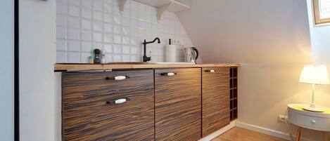 A kitchen with a wooden cabinet, a white tiled backsplash, and a small table with a lamp.