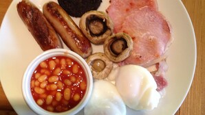 A plate with various breakfast items including sausages, mushrooms, ham, beans, and eggs. - Hazelbank (Uig)