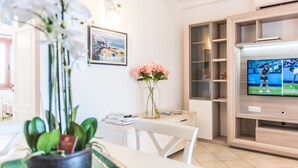Una sala de estar moderna con televisor, una mesa de comedor y un jarrón con flores.