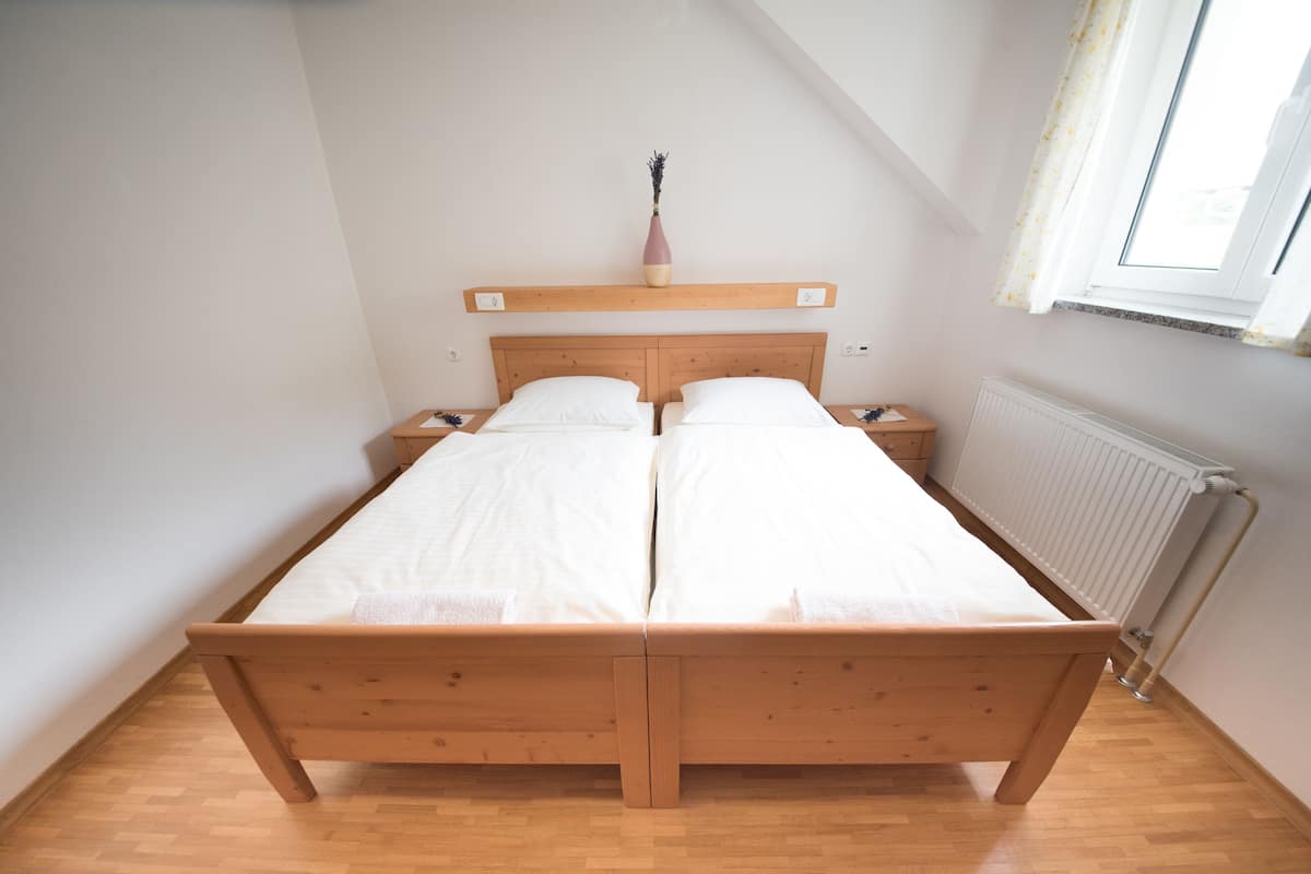 Un lit double avec un cadre en bois, deux tables de chevet, une petite table et un vase posé sur une étagère au-dessus du lit.