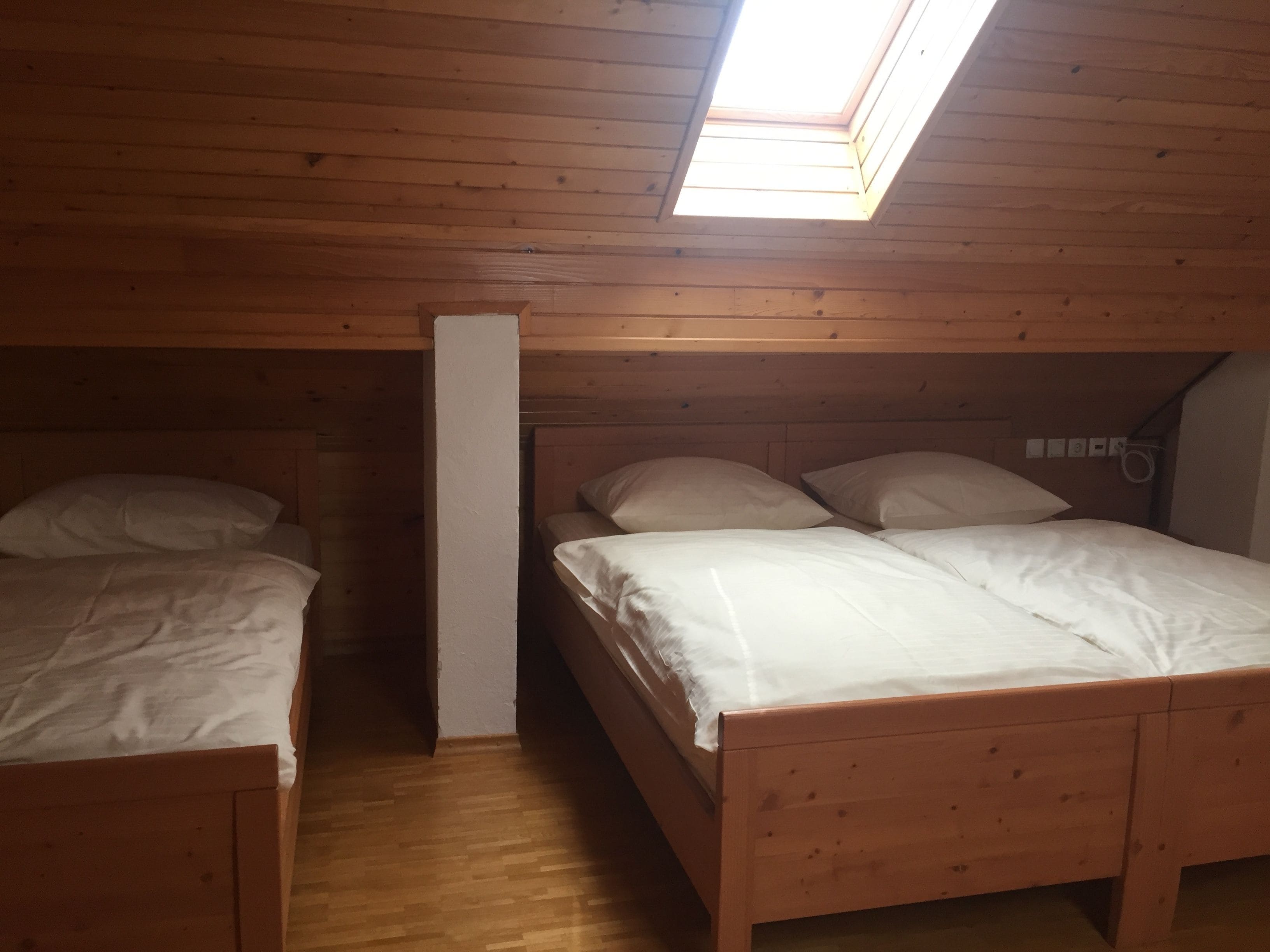 Een kleine, houten kamer met twee bedden, een dakraam en een witte muur.
