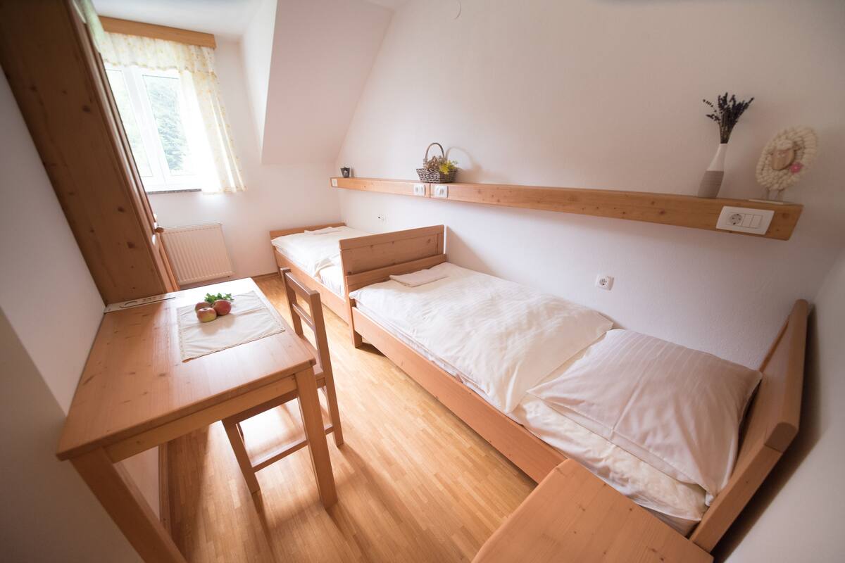 Un petit logement composé d’une seule pièce, comprenant un lit en bois, un bureau et une étagère ornée d’objets décoratifs.