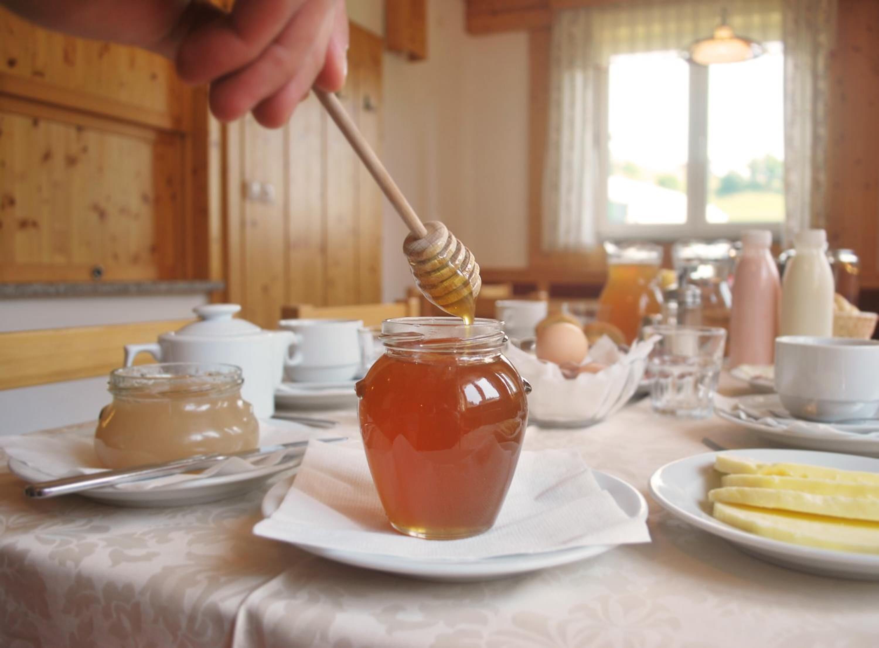 A breakfast setting with a jar of honey, a honey dipper, eggs, and various breakfast items on a table.