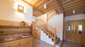 Una escalera de madera que lleva al segundo piso, armarios de madera con revistas, y un aplique en la pared.