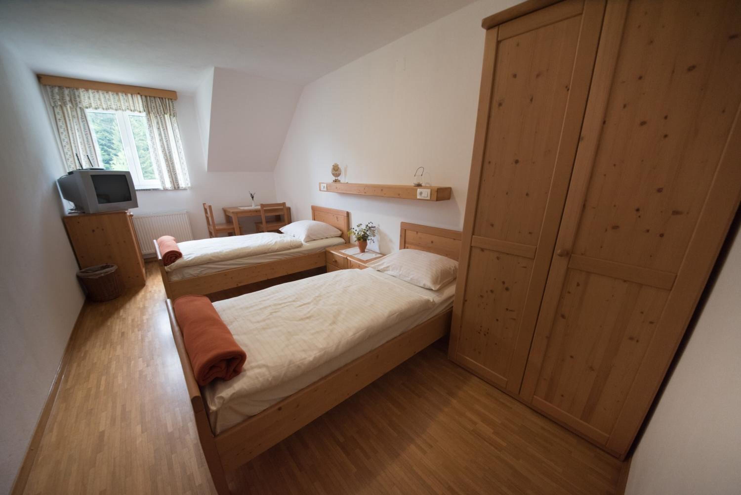 Une chambre à coucher avec deux lits en bois, une armoire en bois, un petit bureau avec une chaise, une télévision et une fenêtre avec des rideaux.