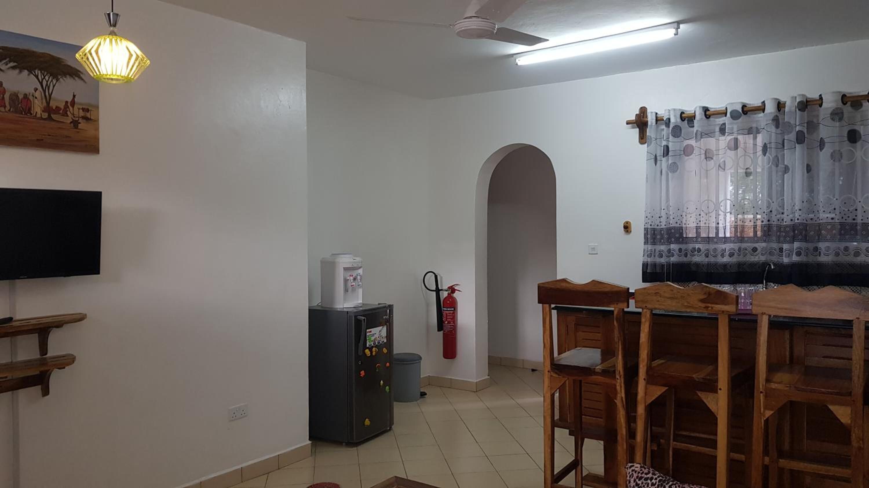 Una sala de estar con una televisión de pantalla plana, una cafetera, un extintor y una mesa de comedor de madera.