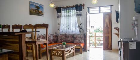 A dining area with wooden furniture, a sofa with patterned cushions, and a view of the outdoors through a door.