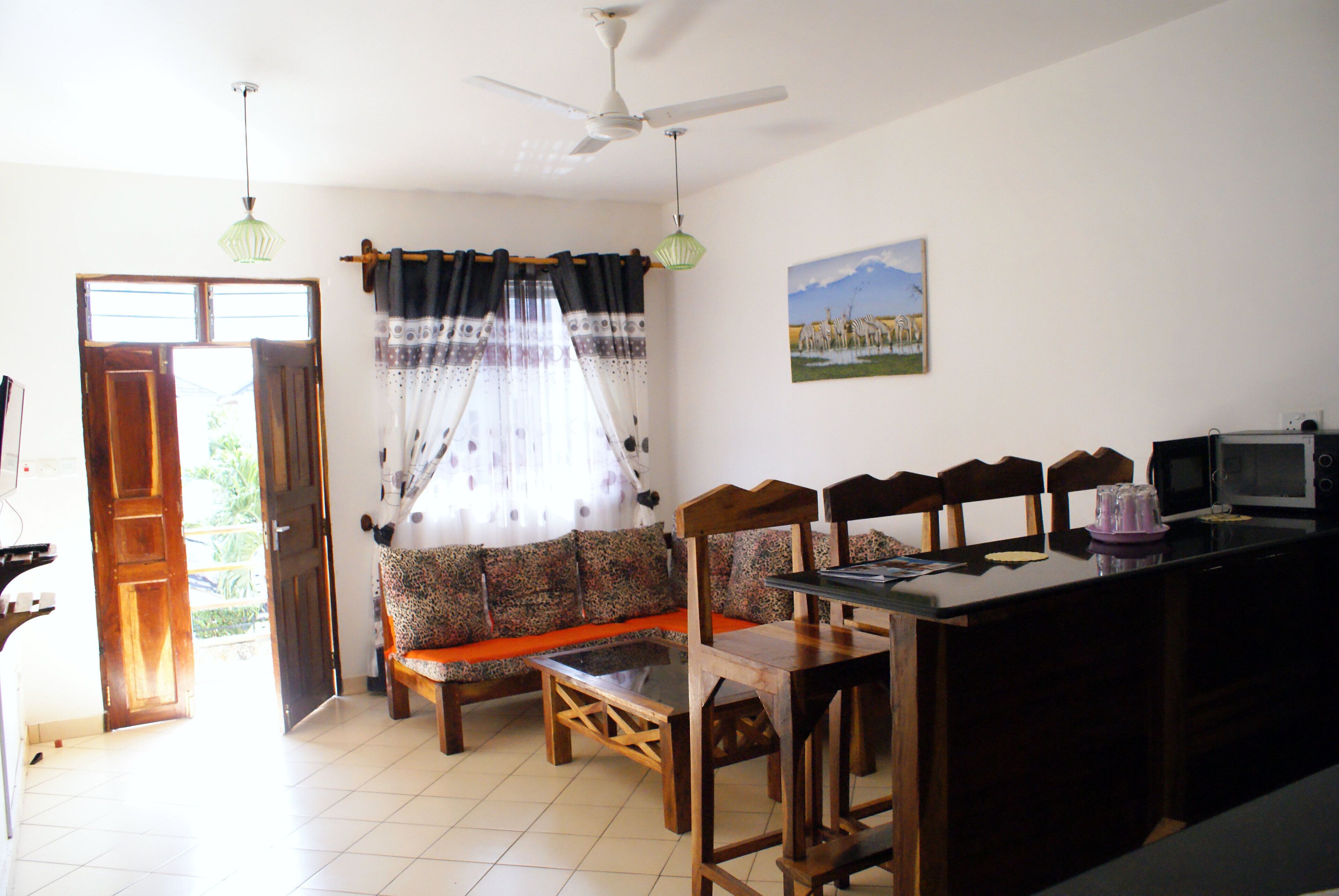 A living room with a sofa, wooden chairs, a dining table, a ceiling fan, and a television.