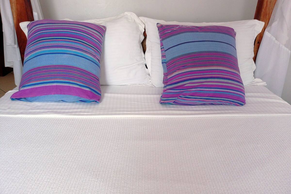 Una cama con ropa blanca y dos almohadas a rayas.