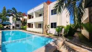A modern two-story building with a swimming pool, surrounded by palm trees and greenery. - Pendo Villas Diani (Diani Beach)