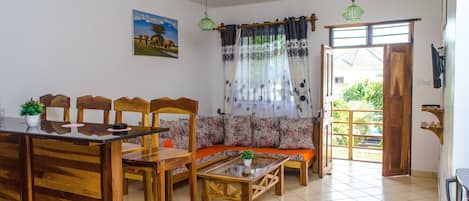 A dining area with wooden furniture, a glass-top table, and a sofa with patterned cushions.