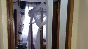 A hallway leading to a bedroom with a bed, a window with curtains, and a tiled floor. - Pendo Villas Diani (Diani Beach)