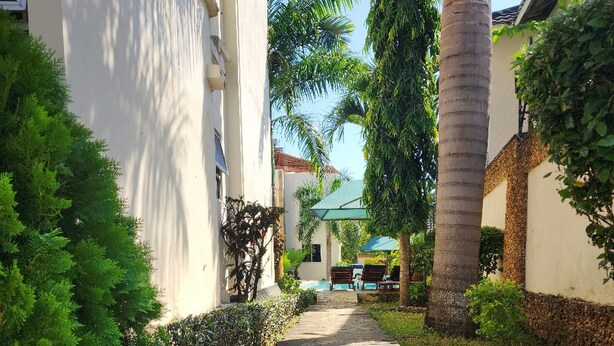 A stone pathway leading to a pool area surrounded by lush greenery and palm trees. - Pendo Villas Diani (Diani Beach)