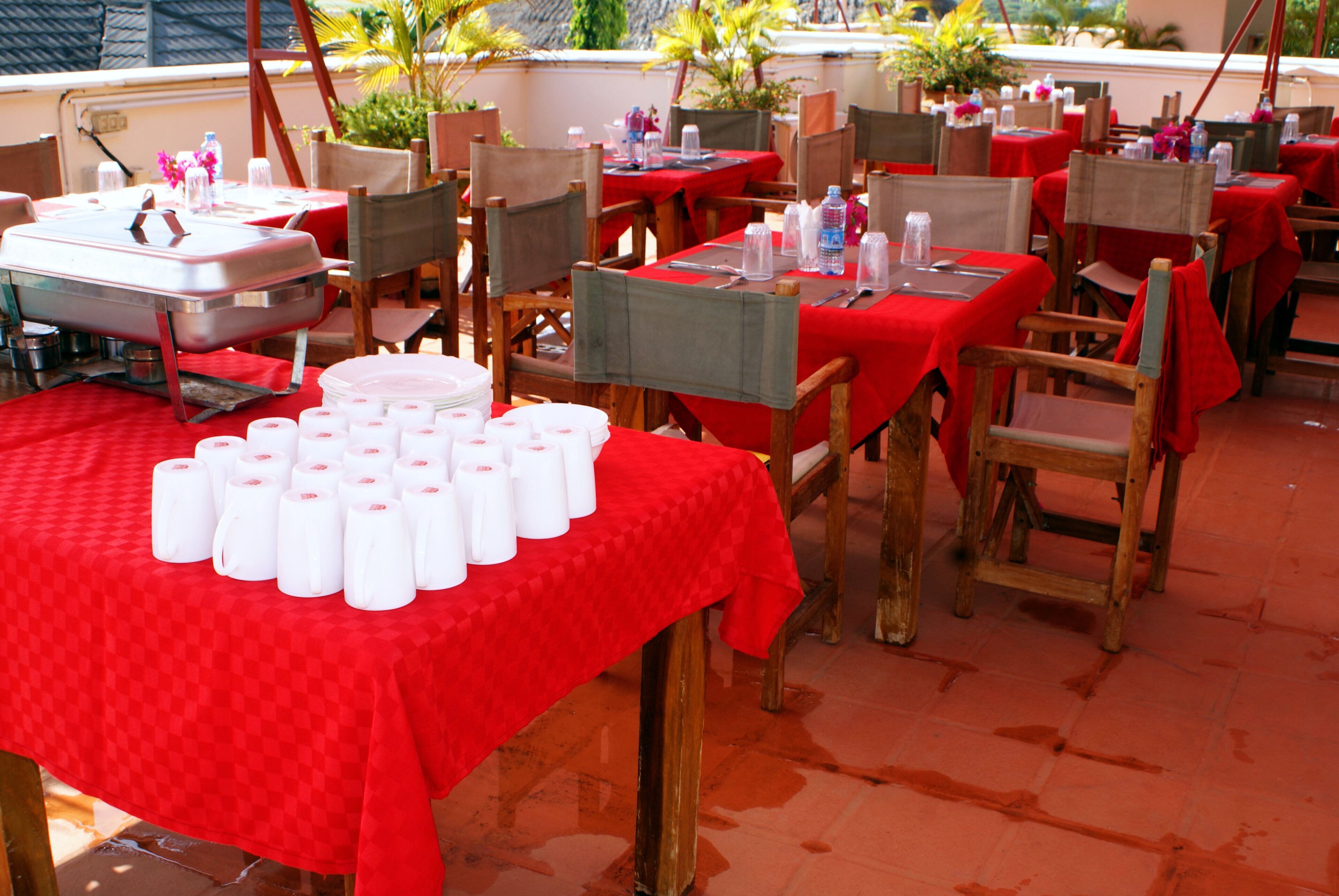 An outdoor dining area with tables covered in red tablecloths and wooden chairs.
