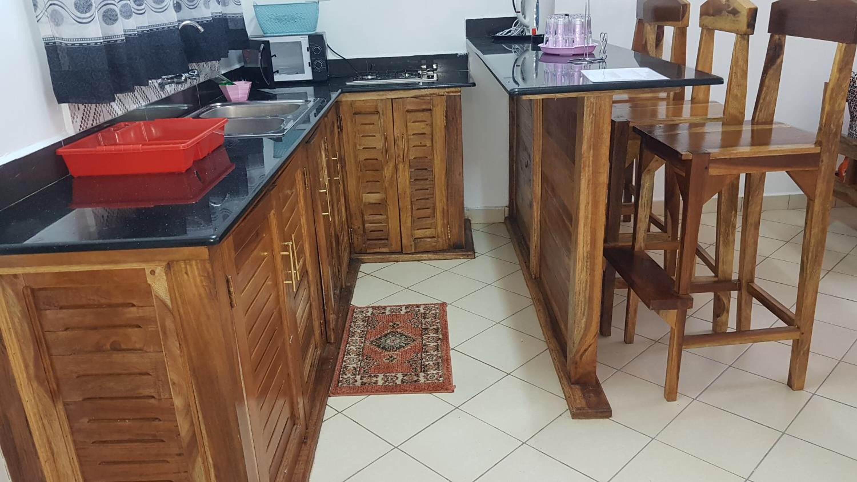 Een keuken met houten kastjes, een zwart aanrecht, een magnetron, een fornuis en een eethoek met een houten tafel en stoelen.