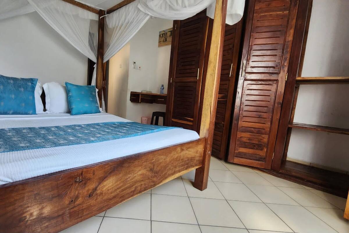 Una cama de madera con dosel, ropa de cama azul y blanca, y piso de baldosas.