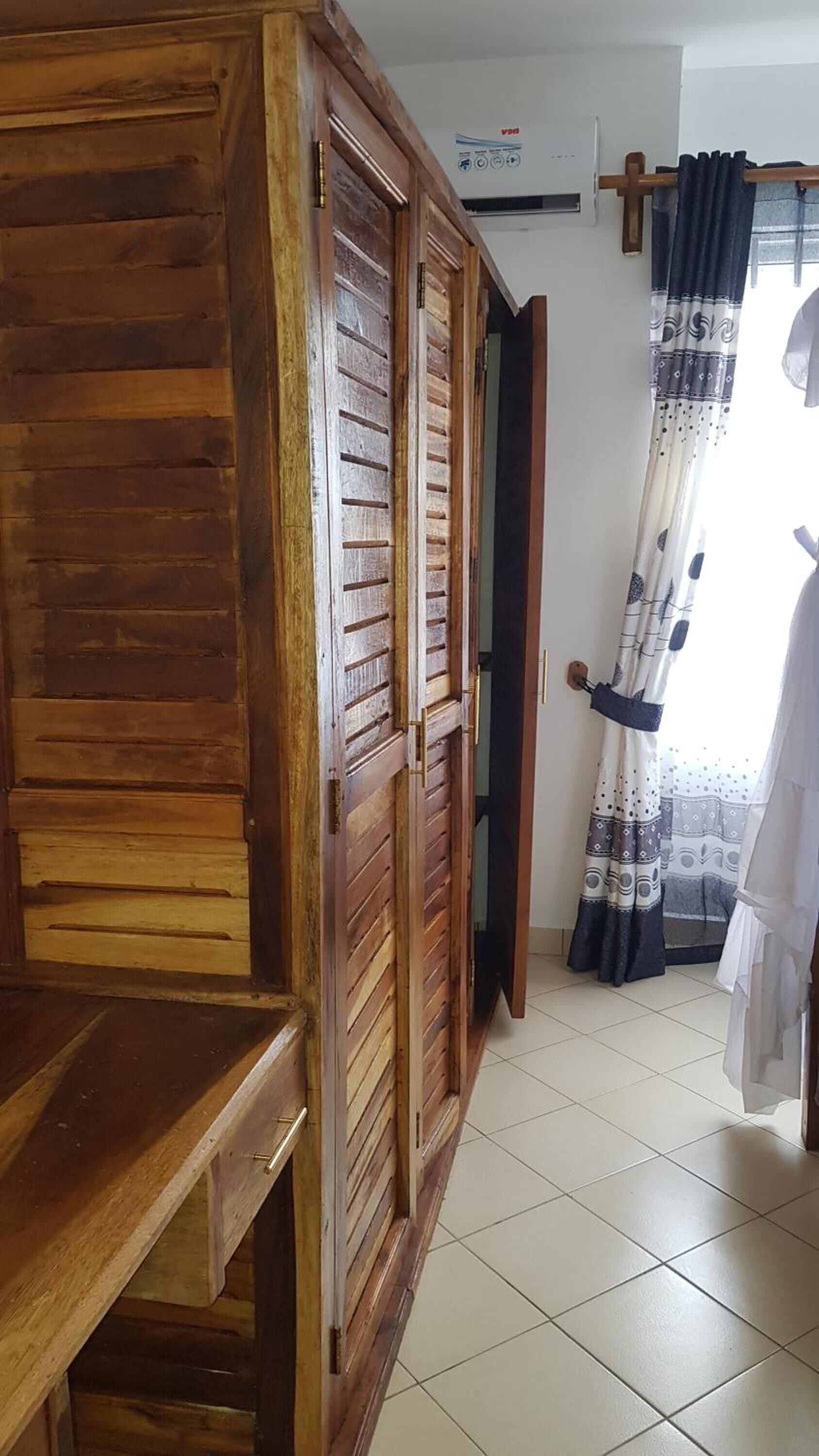 A room with a wooden wardrobe, a tiled floor, and a curtain with a pattern.