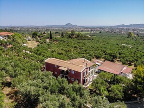 Ein großes, rot-zippelstein-gebautes Gebäude mit mehreren Etagen und Balkonen, umgeben von dichtem Grün und einer hügeligen Landschaft im Hintergrund.