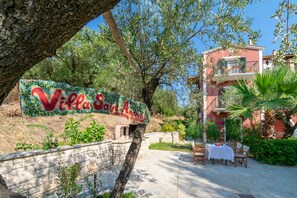 Een villa, genaamd 'Villa Saint Andreu', met een bord, terrasmeubilair en een stenen muur.