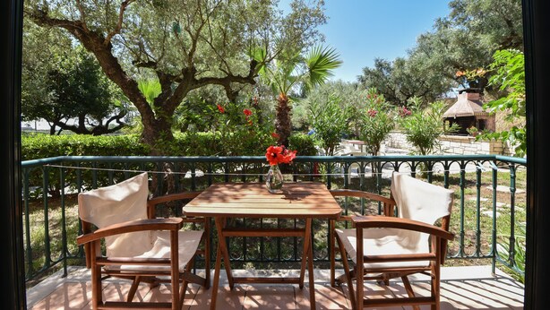 A wooden table with two chairs and a vase of flowers on a balcony with a metal railing. - Villa San Andreas (Zakynthos)