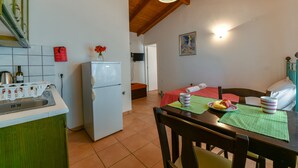 A compact kitchen with a refrigerator, a sink, and a dining area with a table and chairs. - Villa San Andreas (Zakynthos)