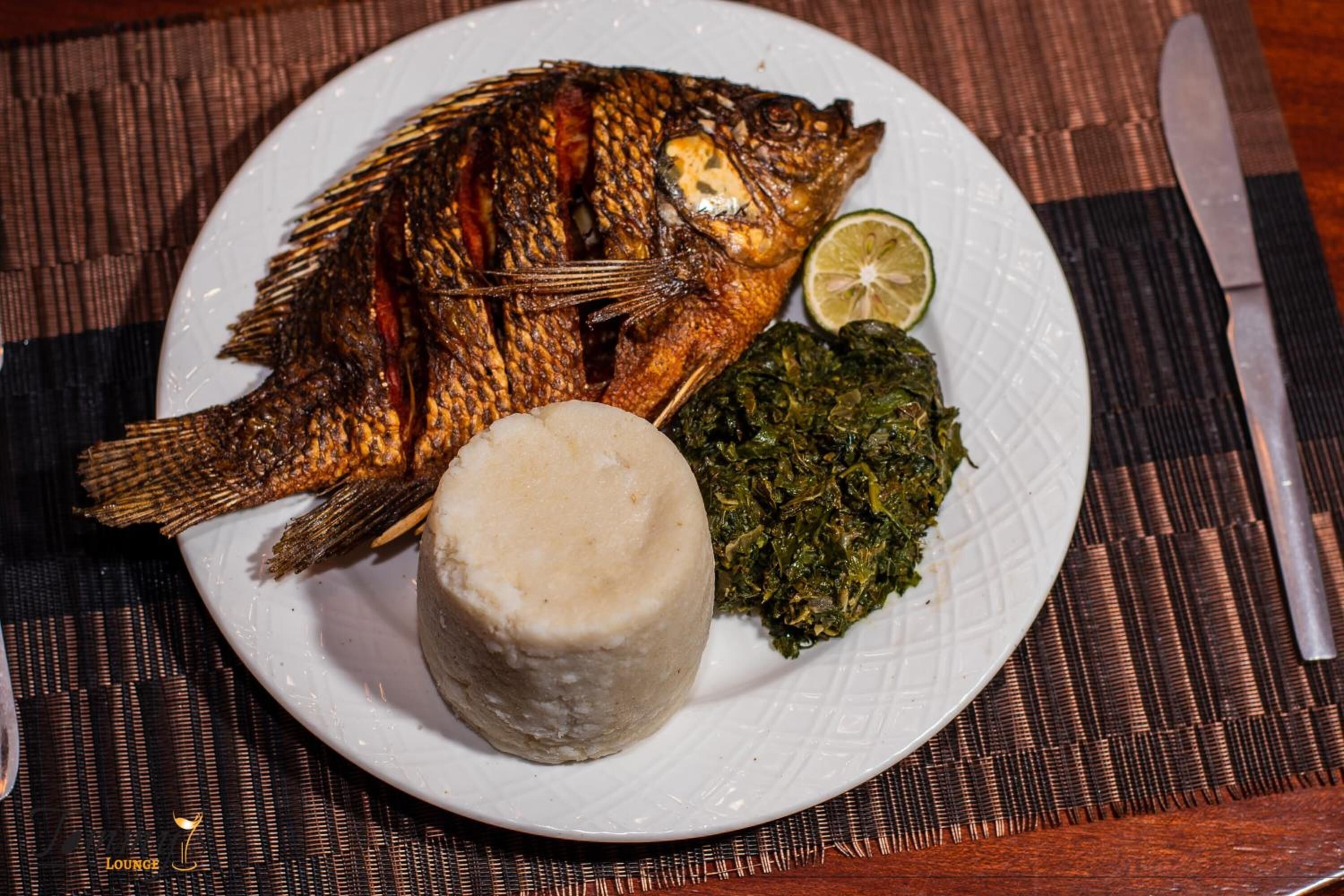 A plate with a whole fish, a lime wedge, and a side of greens.