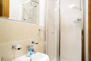 A modern bathroom with a glass-enclosed shower, a white sink with a mirror above it, and a towel rack. - JOIVY 5 Bedroom Apt Near Meadows & George Square (Edinburgh)