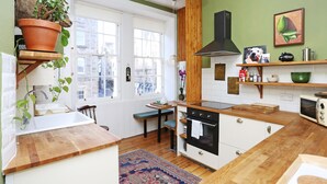 A kitchen with a wooden countertop, white cabinets, a built-in oven, and a hanging plant. - JOIVY Old Town Gem - Apartment With Great City Views (Edinburgh)